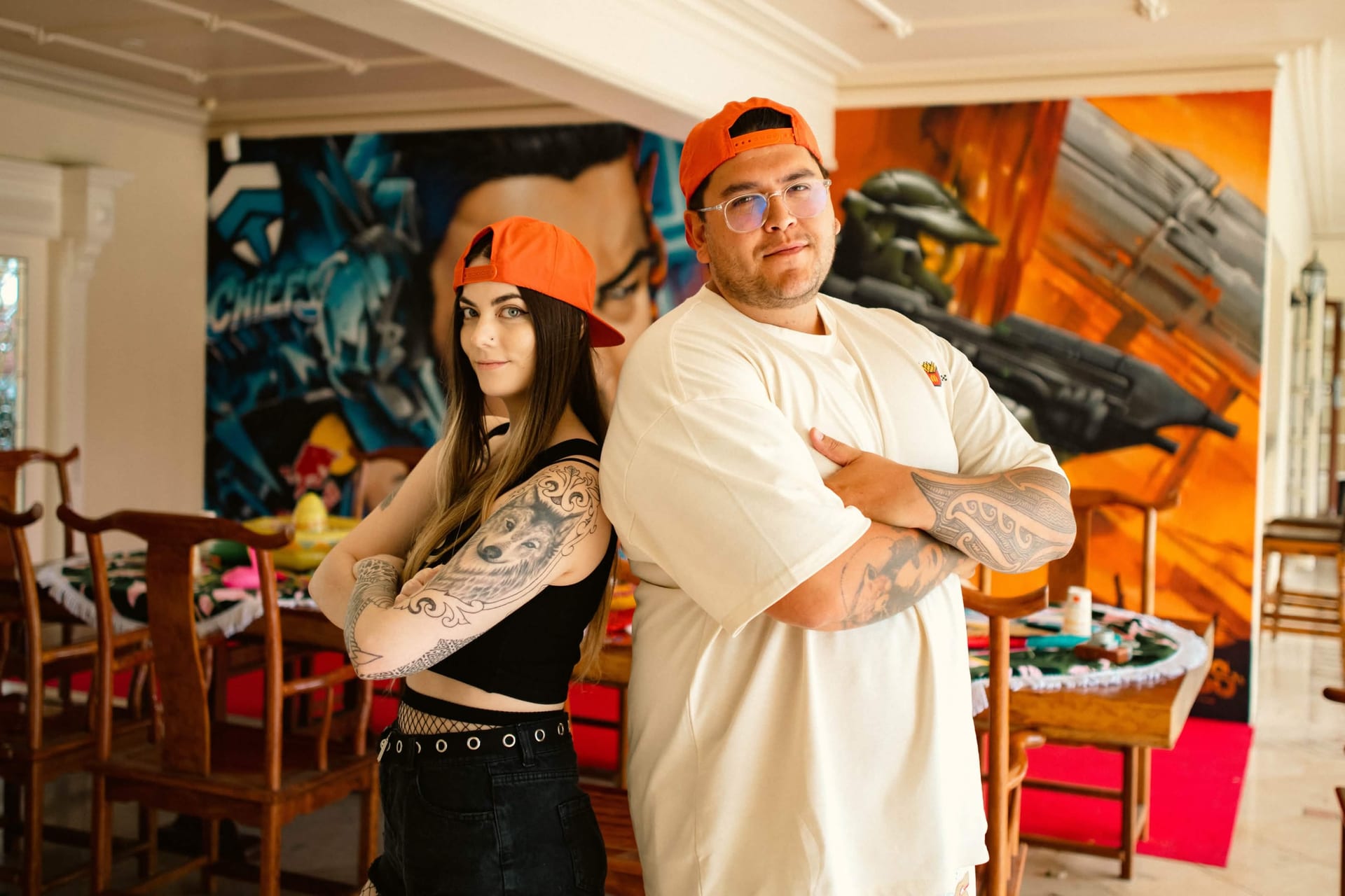Two creators back to back in McDonald's x Chiefs caps in front of the Chiefs mansion mural
