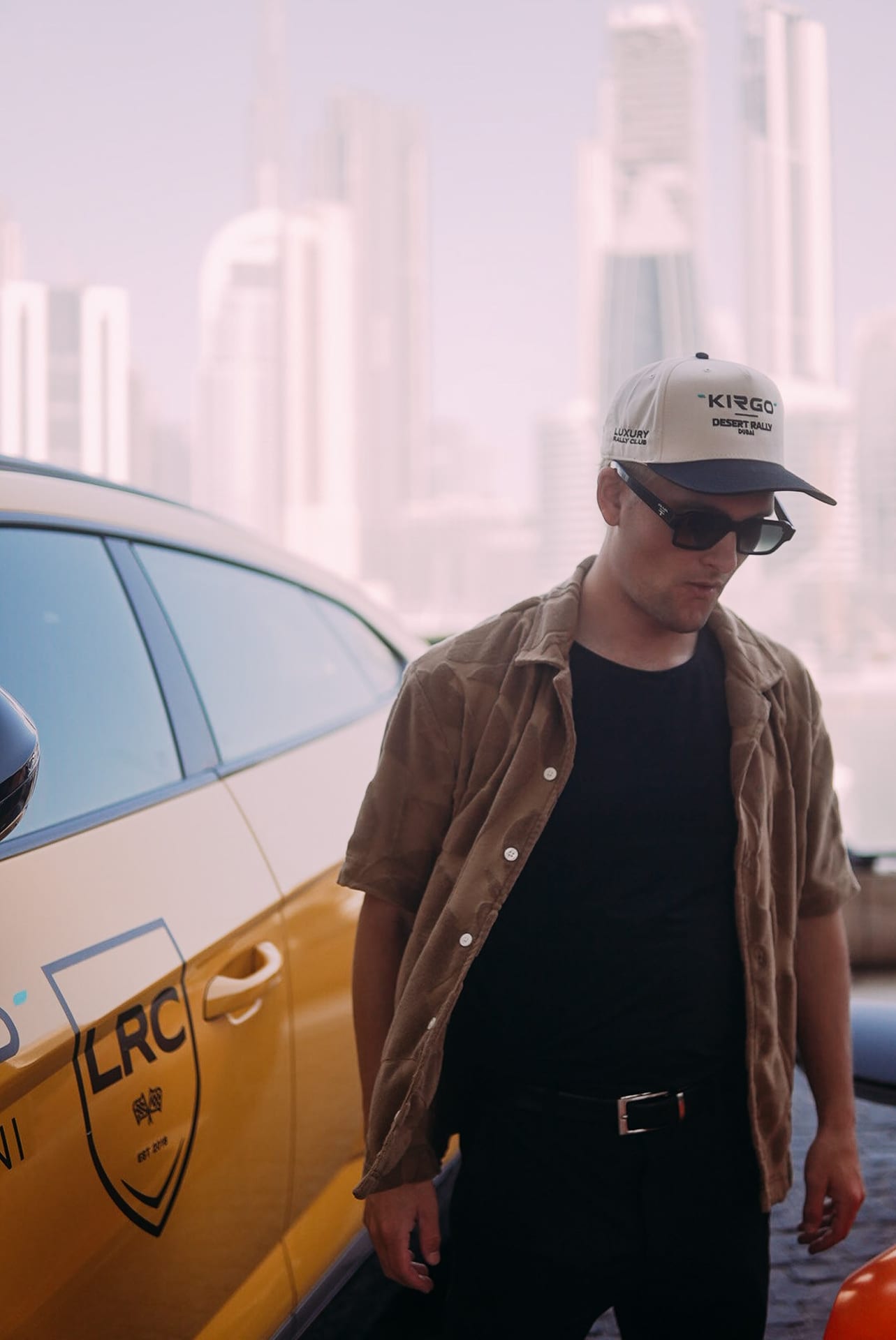 Luxury Rally Club participant beside a branded rally car with the Dubai skyline behind
